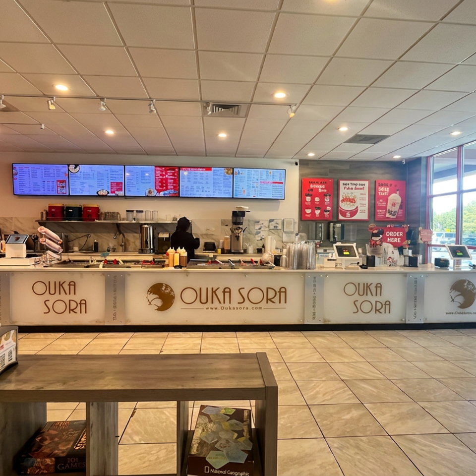 Bright Ouka Sora restaurant interior with sushi counter, digital menus, promotional posters, and large windows overlooking the parking lot.