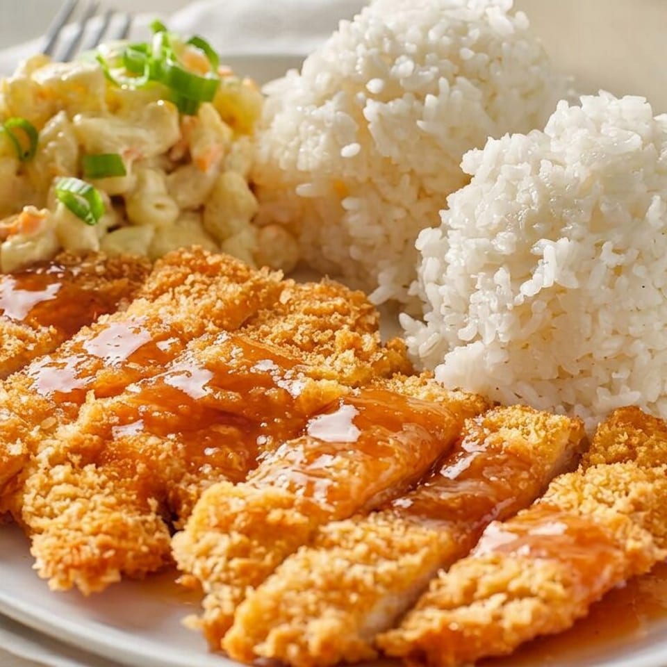 Breaded chicken cutlets drizzled with sauce, served with white rice and creamy vegetable salad on a plate.