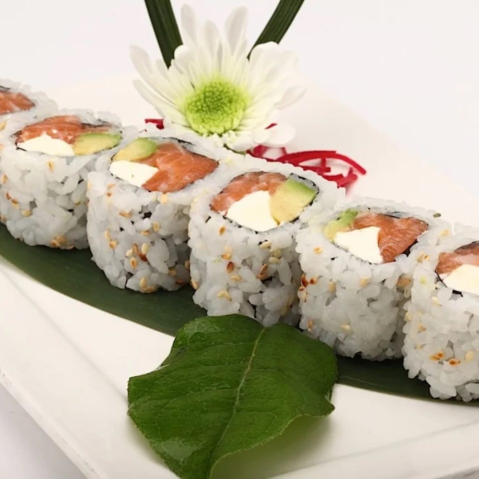 Salmon, avocado, and cream cheese sushi rolls on a white platter.
