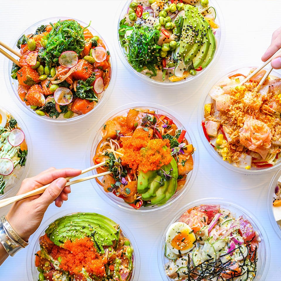 An overhead spread of colorful bowls with avocado, vegetables, and seafood.