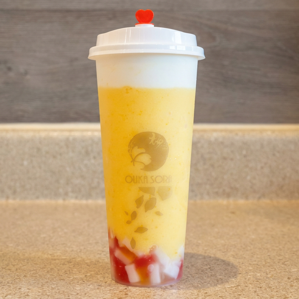 Yellow fruit smoothie with red and white fruit pieces in a lidded Ouiça Sora cup on a wooden counter.