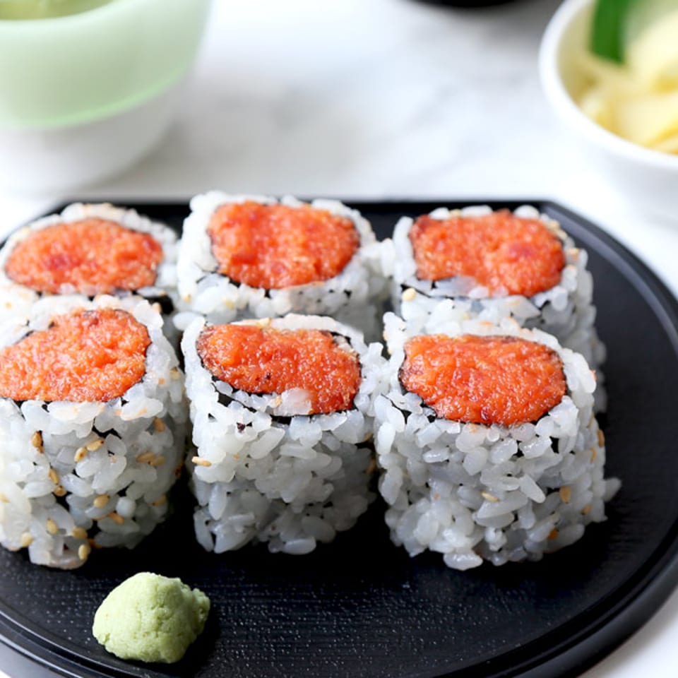 Six sushi rolls with orange filling and wasabi on a black plate.